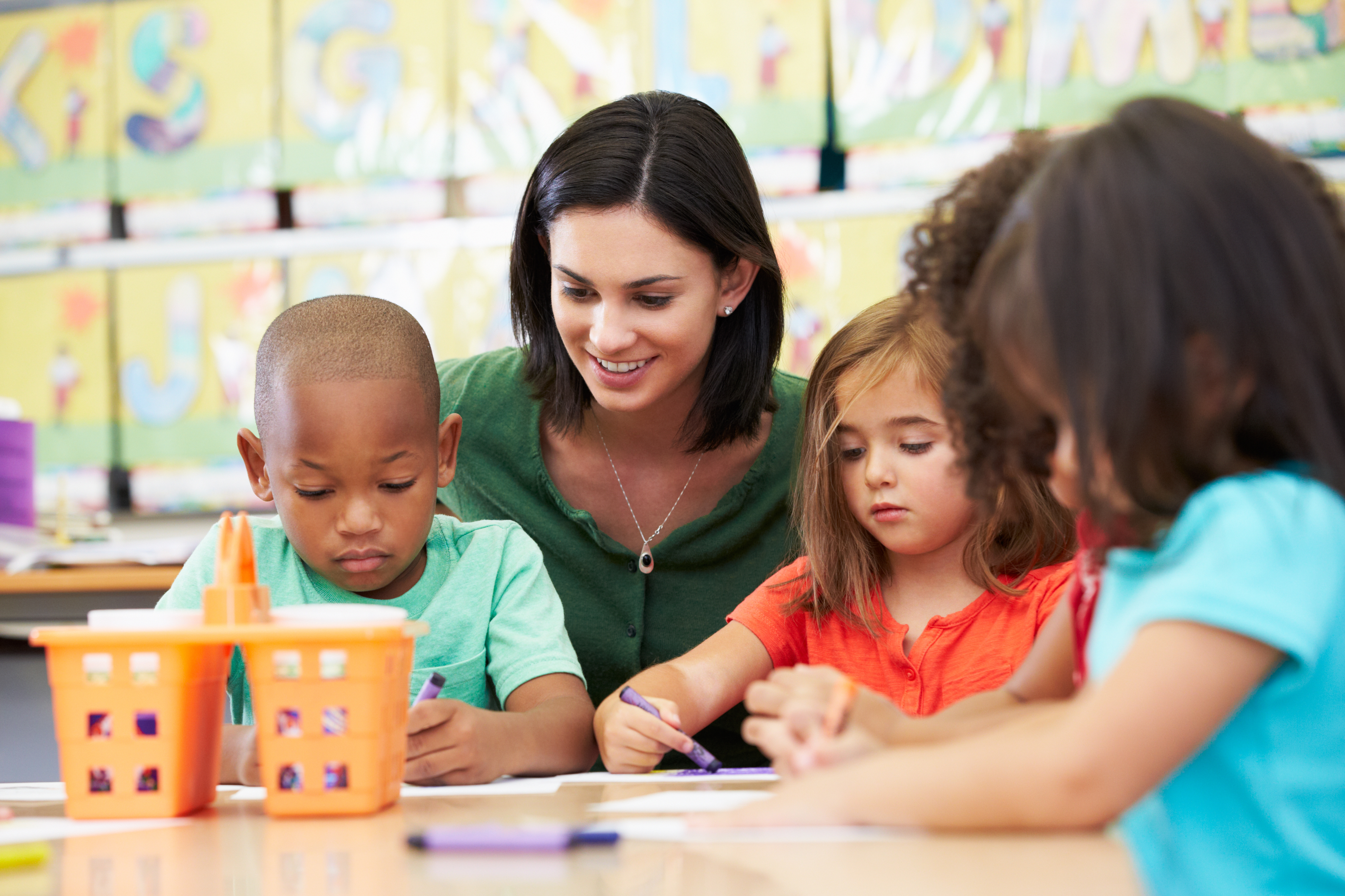 Four children coloring with an adult in a classroom
