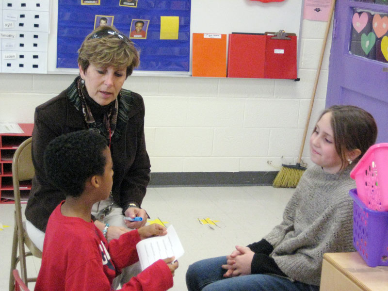 Mrs. Lynnie McCrobie, Director of Community Options with Middle Penninsula
Community Services Board, assists two students practicing a social exchange
during the after school social skills club held at Lancaster Primary School