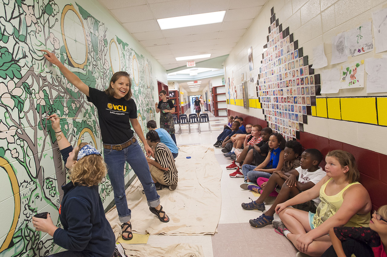 Teachers and students painting mural in school hall
